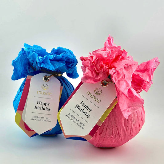 Two bath bombs, one blue and one pink, with 'Happy Birthday' tags on a light gray background.