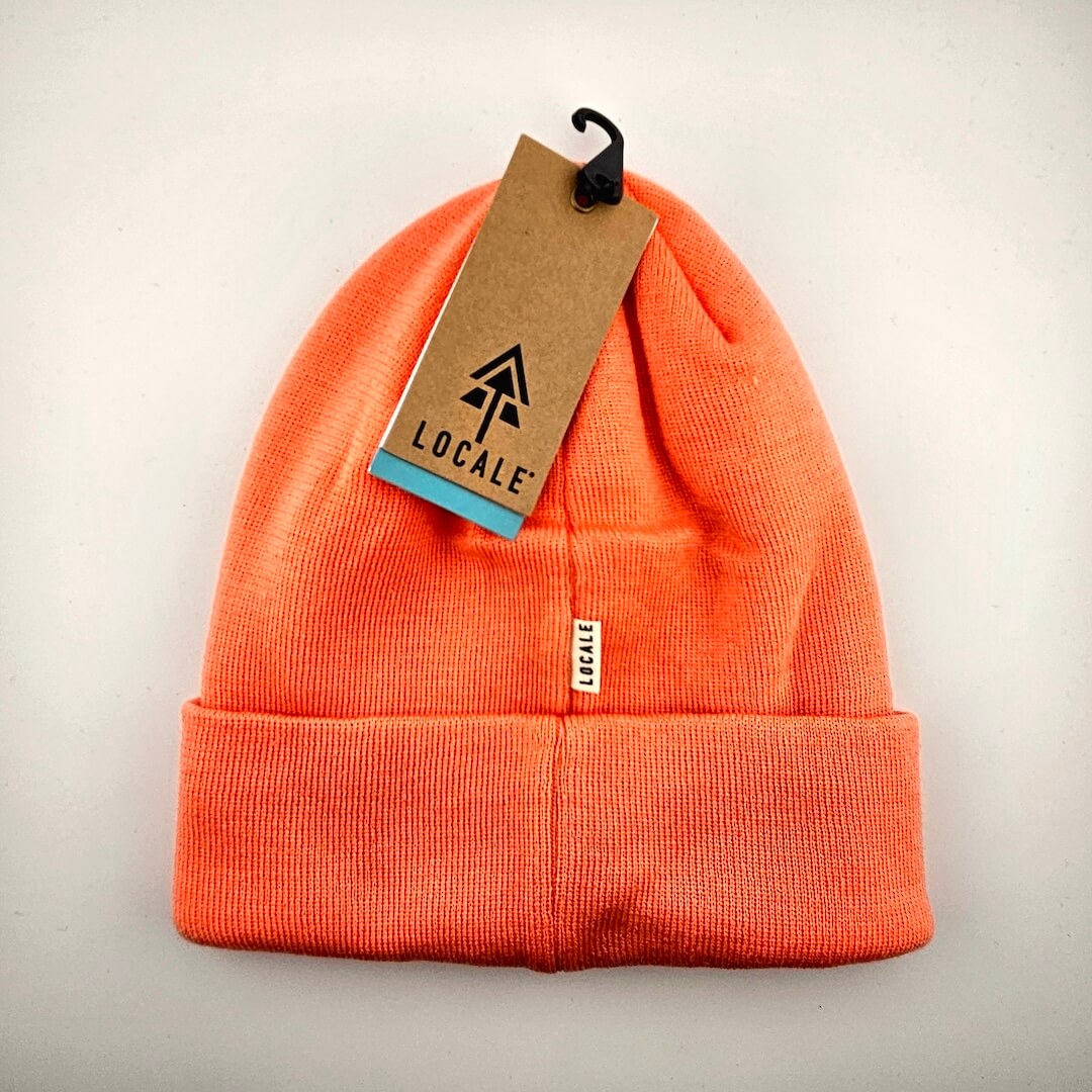 Salmon pink beanie with a 'Locale' tag on a light gray background