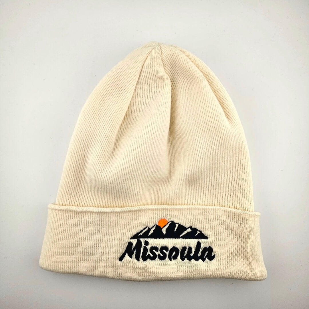 Beige beanie with 'Missoula' and mountain design on a gray background