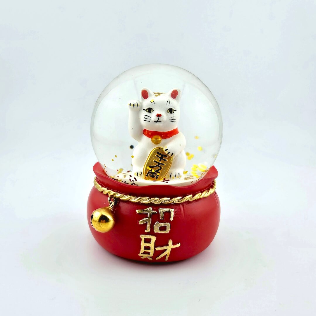 Decorative snow globe with a cat figurine and red base on a white background
