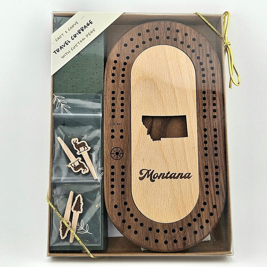 Wooden cribbage board with state silhouette in center above, "Montana" in curvy print, 2 sets of 2 pegs, trees & deer topped