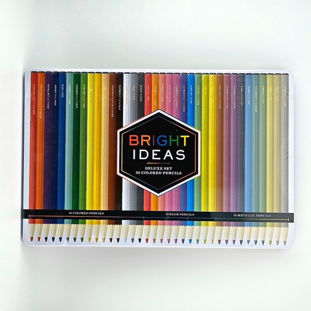 White tin with colored pencils in rainbow pattern on lid against white background. 