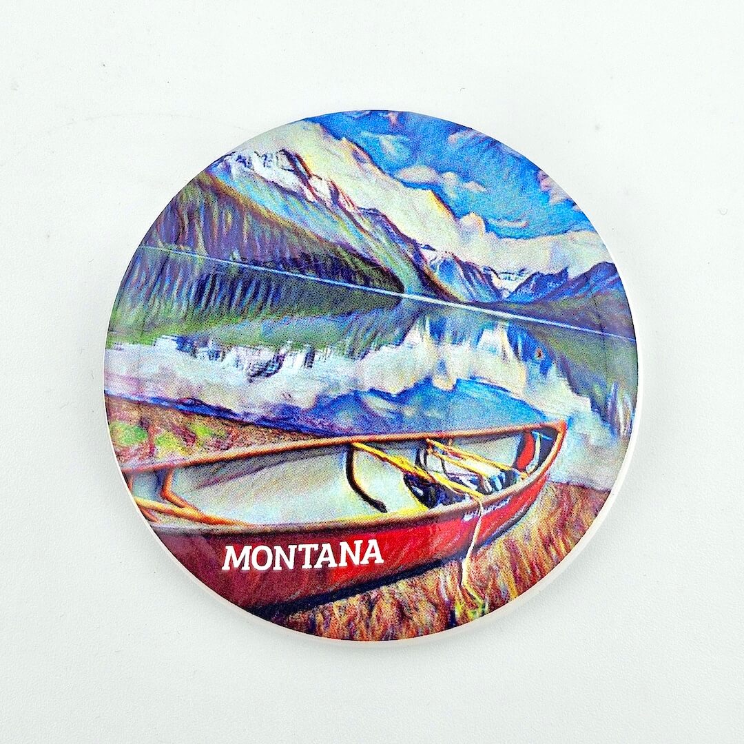 Round coaster with a scenic design of a lake and mountains, featuring a red canoe labeled 'Montana'.