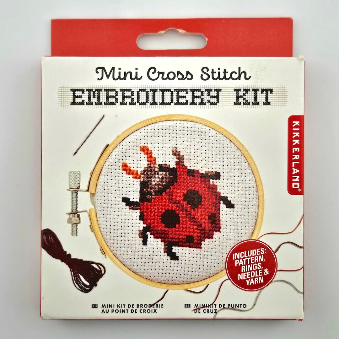 Mini Cross Stitch kit featuring lady bug pattern with white and red packaging against white background. 