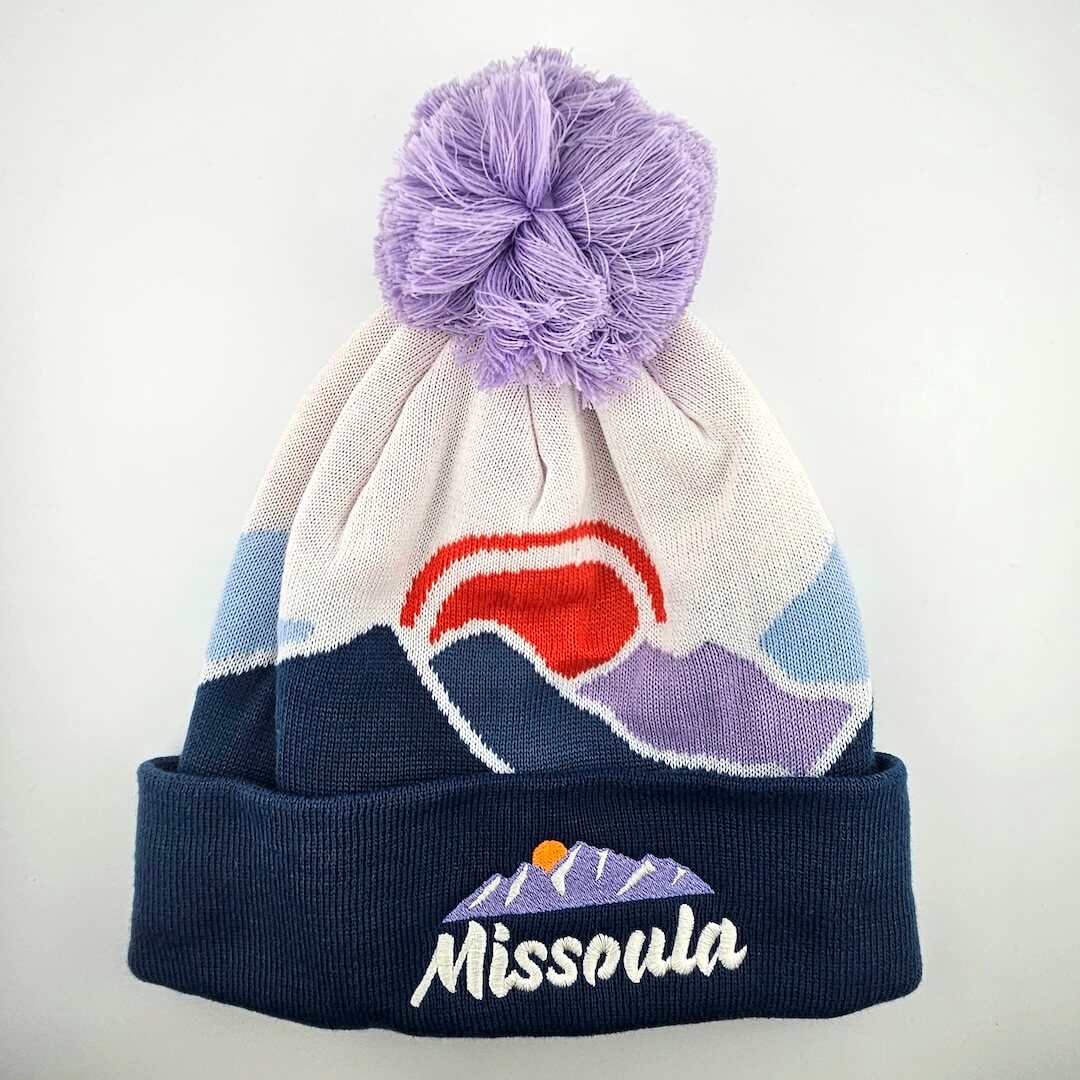 Beanie with purple pom-pom, colorful design, and 'Missoula' branding on a white background