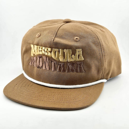 Brown canvas hat with "MISSOULA, MONTANA," in wavy block letters across face. White cord sitting on top of brim against face. 