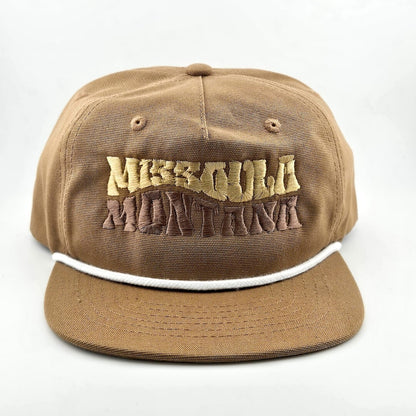 Brown canvas hat with "MISSOULA, MONTANA," in wavy block letters across face. White cord sitting on top of brim against face. 