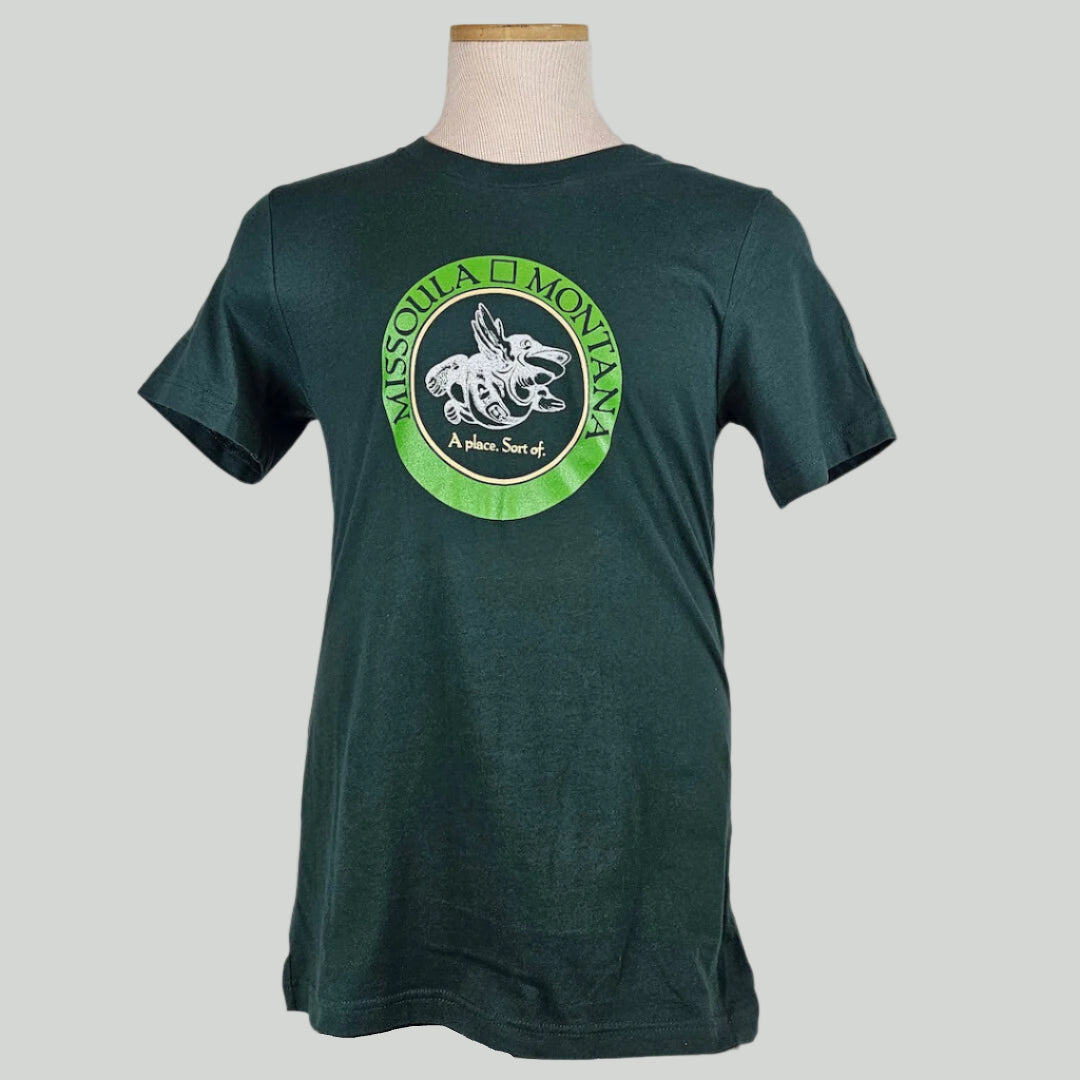 Green shirt with circle in chest with "Missoula, Montana" in band, center of circle has winged frog image & "A place. Sort of."