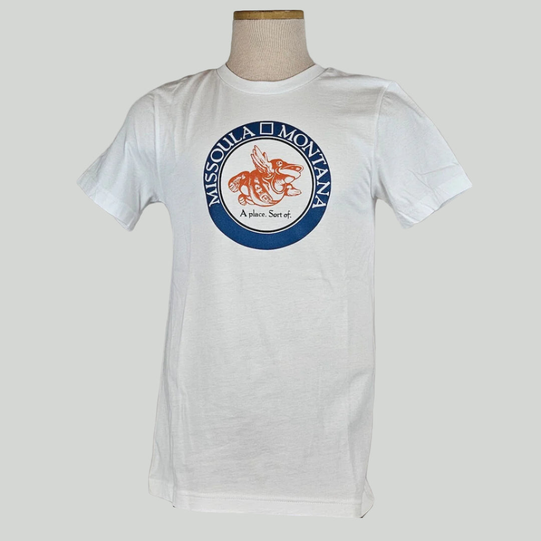 White shirt with circle in chest with "Missoula, Montana" in band, center of circle has winged frog image & "A place. Sort of."
