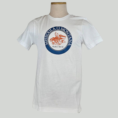 White shirt with circle in chest with "Missoula, Montana" in band, center of circle has winged frog image & "A place. Sort of."