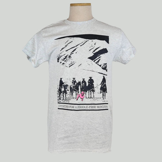 Gray shirt with mountain landscape behind group of mounted cowboys herding pink poodle with lassos. Caption under image. 