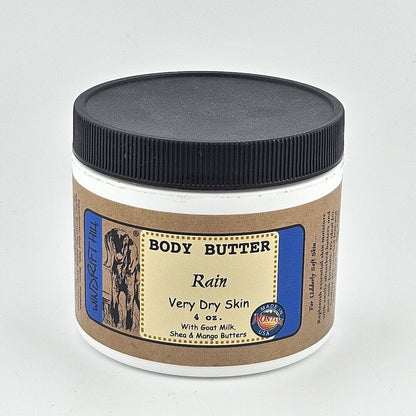 Jar of body butter labeled 'Rain' for very dry skin on a gray background