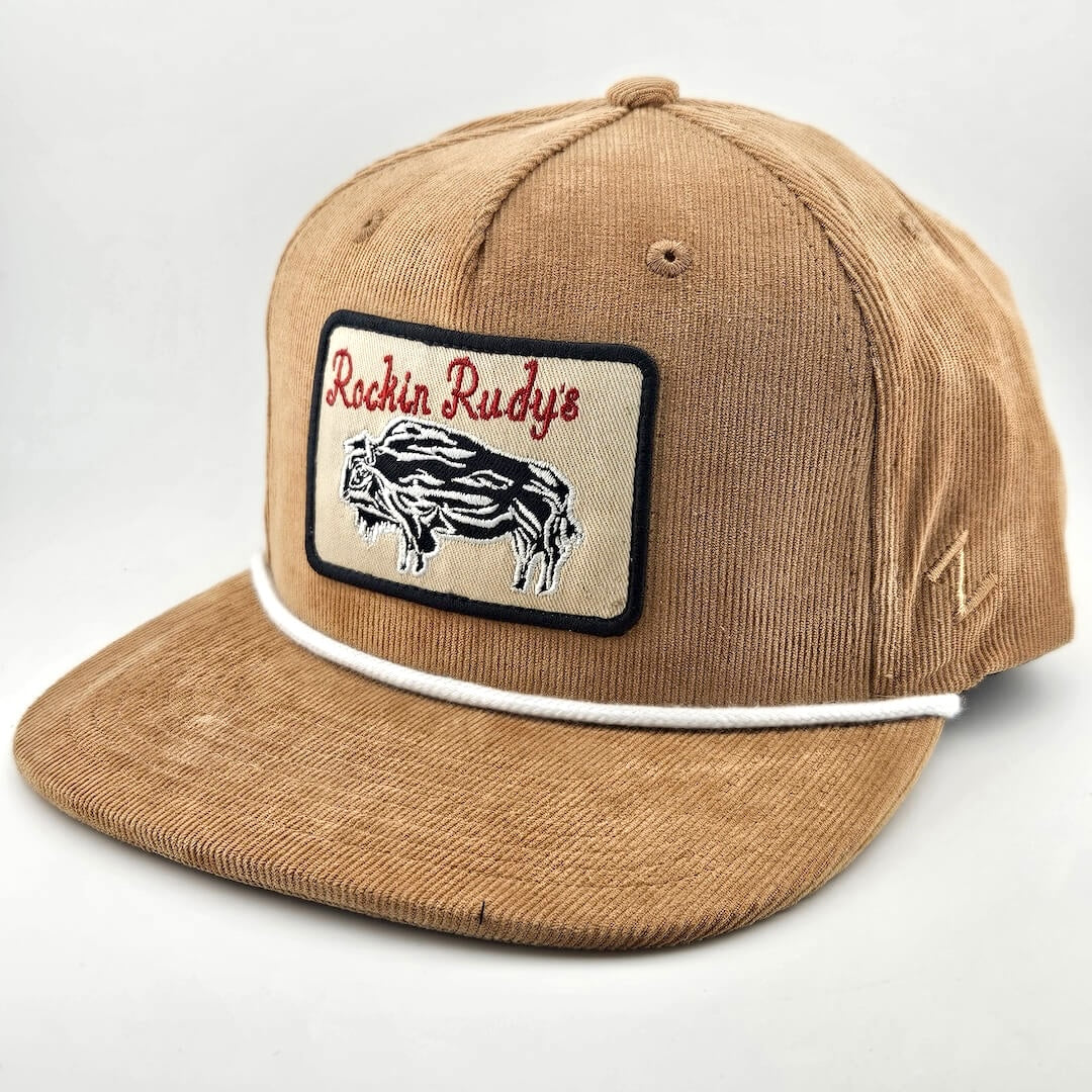 Brown corduroy had with patch on face with bison silhouette below "Rockin Rudy's" in curly script. White cord rest on brim. 