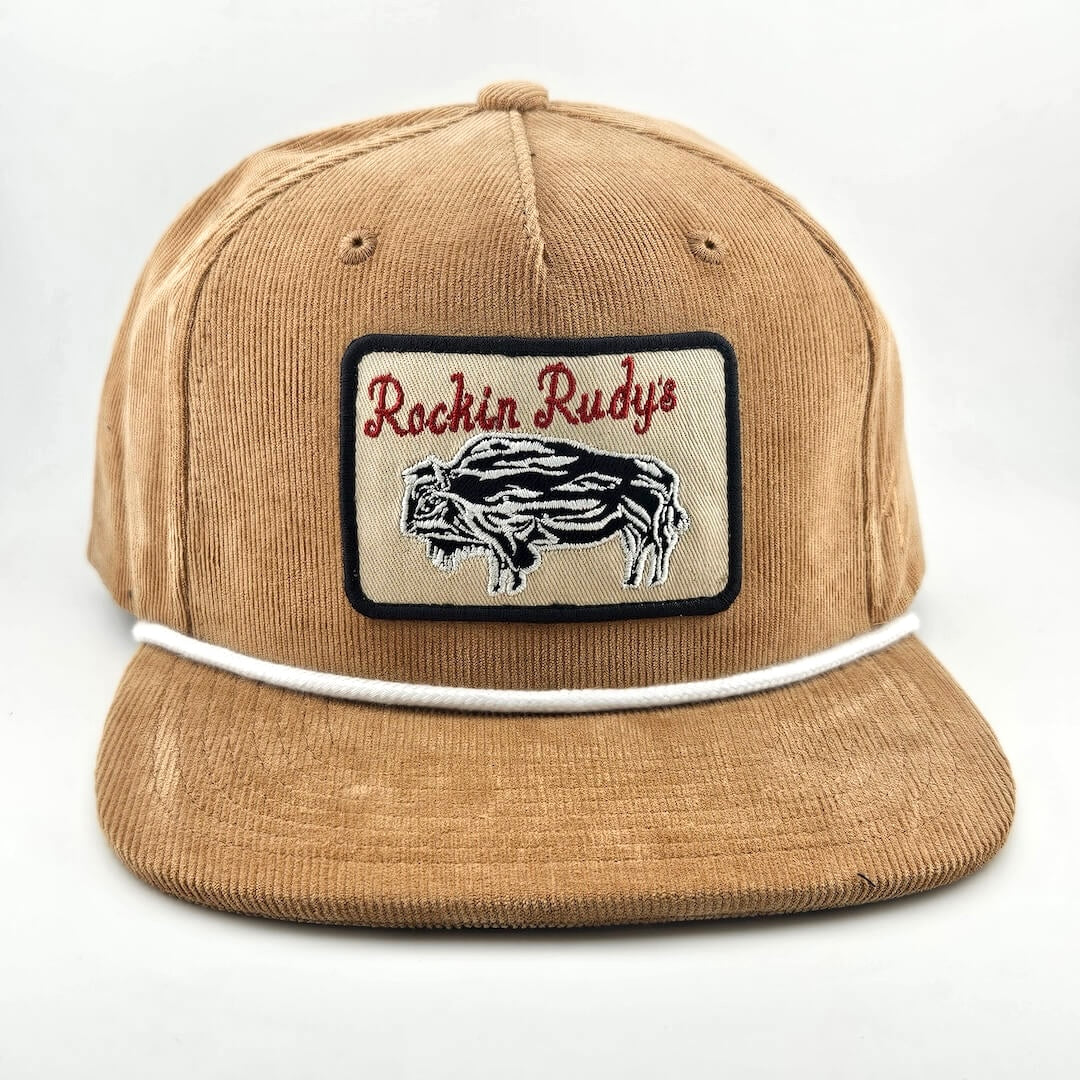 Brown corduroy had with patch on face with bison silhouette below "Rockin Rudy's" in curly script. White cord rest on brim. 