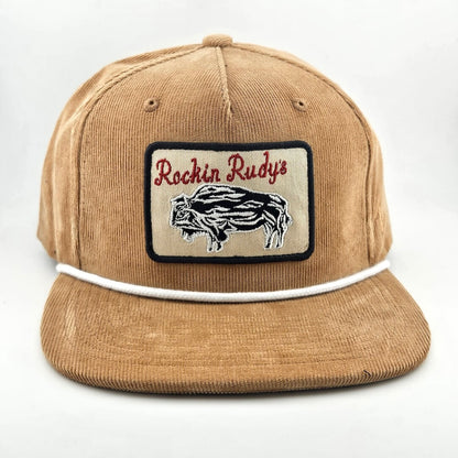 Brown corduroy had with patch on face with bison silhouette below "Rockin Rudy's" in curly script. White cord rest on brim. 