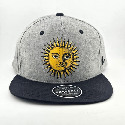 Front of grey heathered hat with black bill and stitching, yellow stylized sun in center of face. 