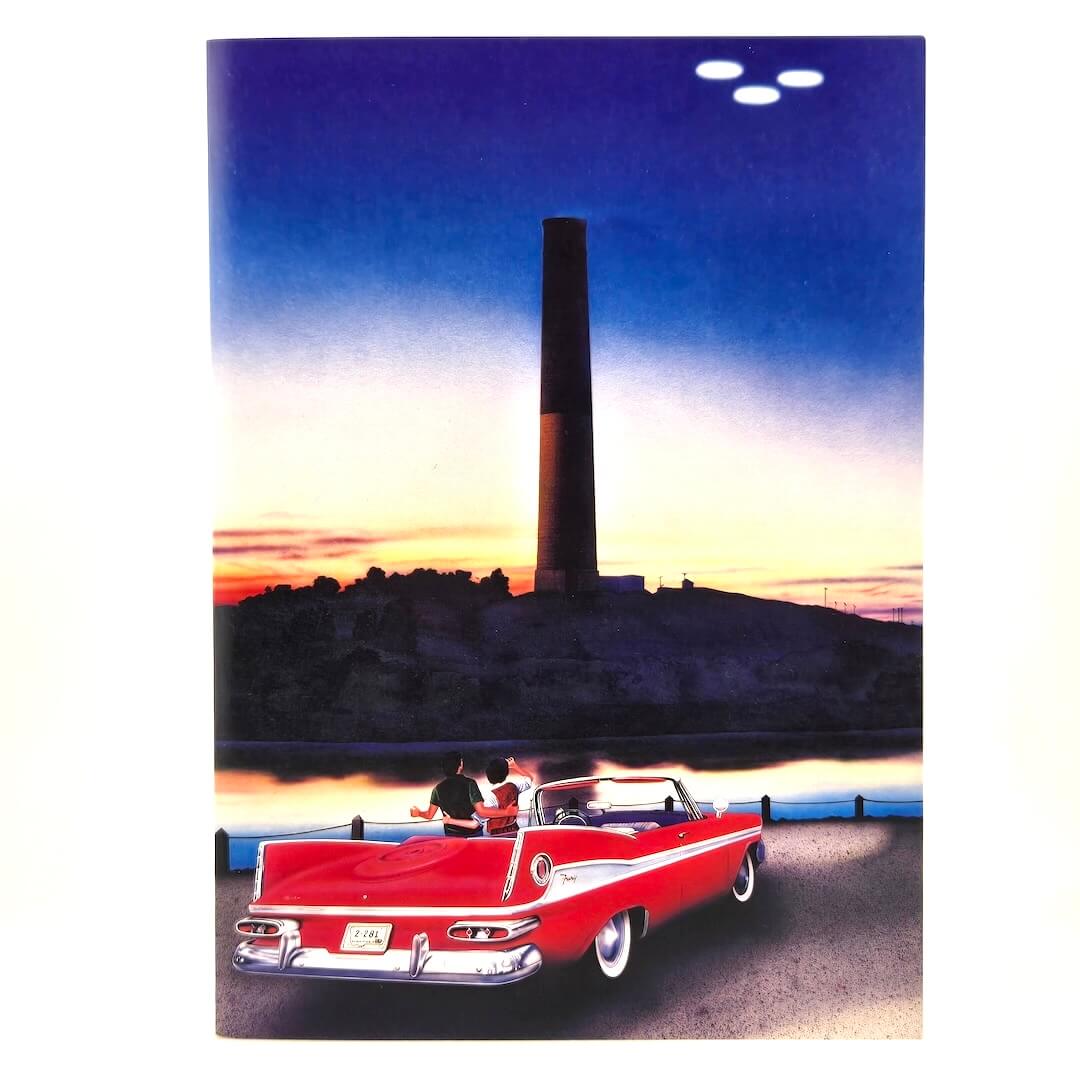 Vintage-style red and white car on a road with a sunset and smoking stack in the background