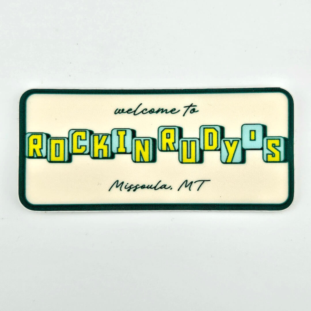 Rectangular sign with 'welcome to Rockin' Rudy's, Missoula, MT' text on a beige background