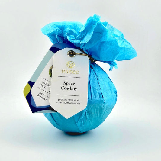 Blue bath bomb with a tag labeled 'Space Cowboy' on a light gray background