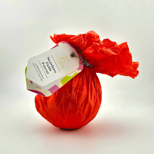 Red wrapped bath bomb with tag against white background. 