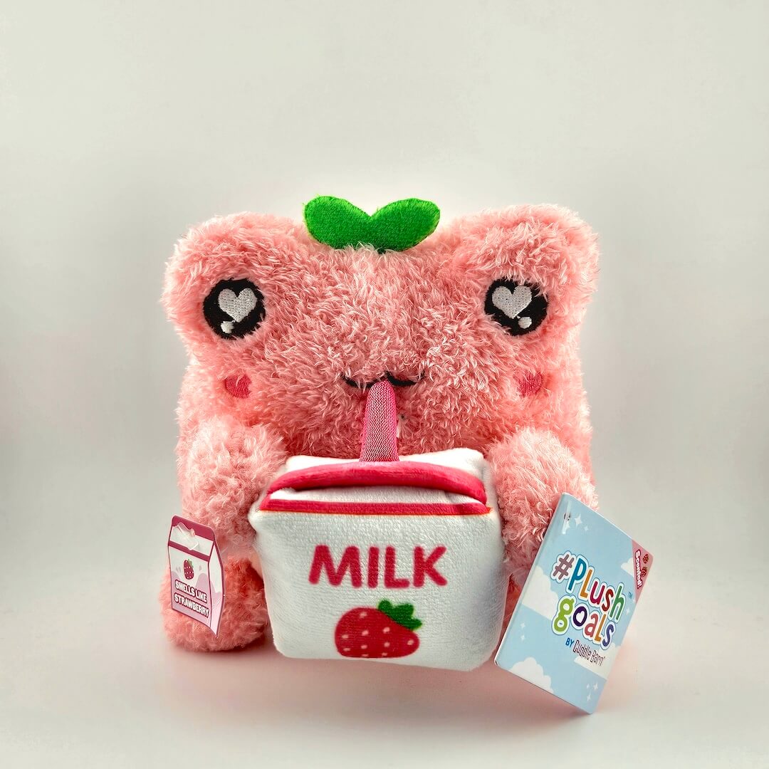 Pink plush toy resembling a strawberry with a milk container, on a light gray background.