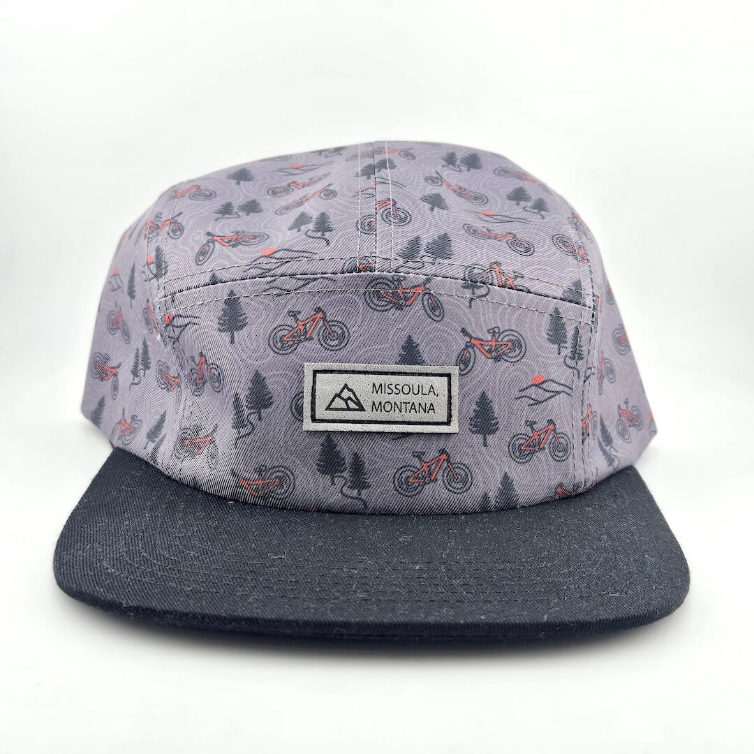 Cap with a pattern of trees, cars, and mountains on a white background