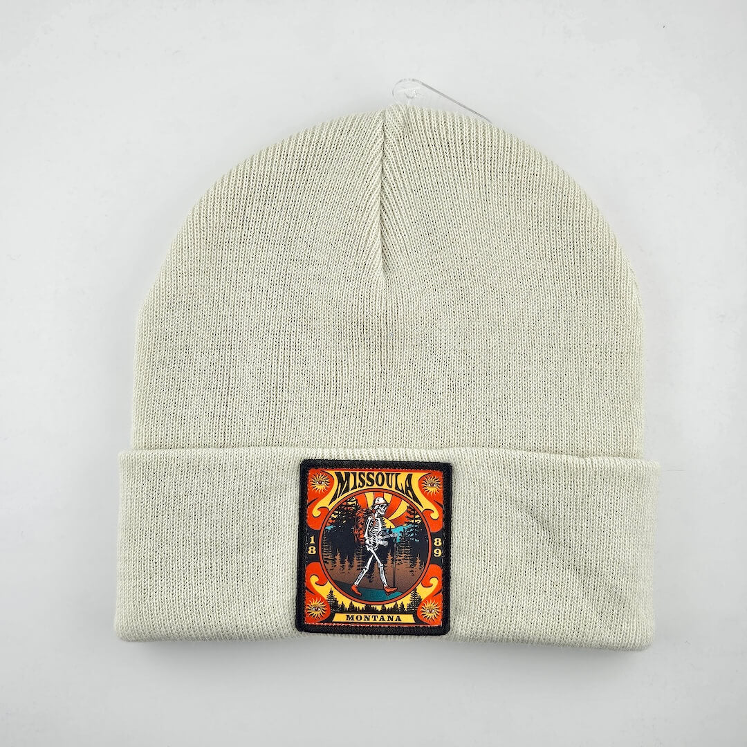 Beige knit beanie with a colorful patch featuring a skeleton and text on a white background