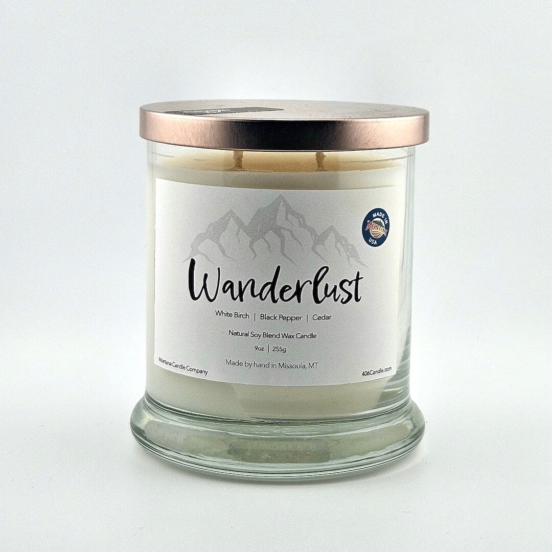 Glass jarred candle with copper lid, label with gray mountain silhouette above printed script  name above scent components. 