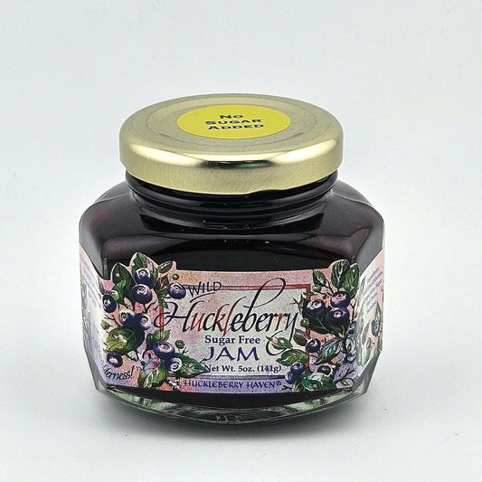 Glass jar with gold lid with, "No sugar added" sticker. Jar label has painting style images of huckleberries & print.