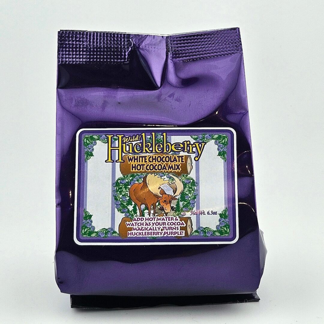 Purple package of Huckleberry white chocolate hot cocoa mix with a label featuring a bear and forest design.