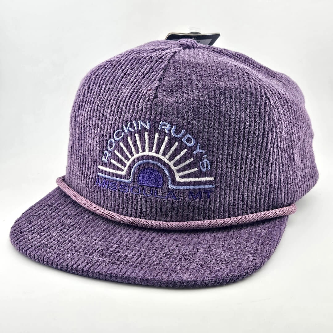 Purple corduroy billed hat with "ROCKIN RUDY'S", radiating from sunburst, "MISSOULA, MONTANA" along horizon bottom.