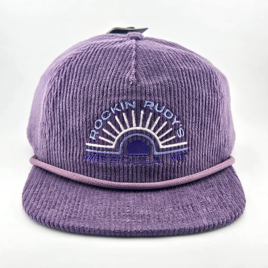 Purple corduroy billed hat with "ROCKIN RUDY'S", radiating from sunburst, "MISSOULA, MONTANA" along horizon bottom.