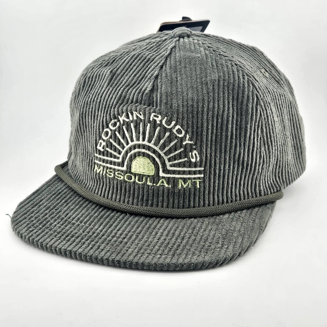 Green corduroy billed hat with "ROCKIN RUDY'S", radiating from sunburst, "MISSOULA, MONTANA" along horizon bottom.