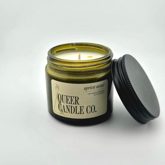 Green glass jar with black lid containing candle with label against white background.