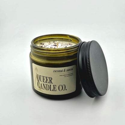 Green glass jar with black lid containing candle with label against white background.