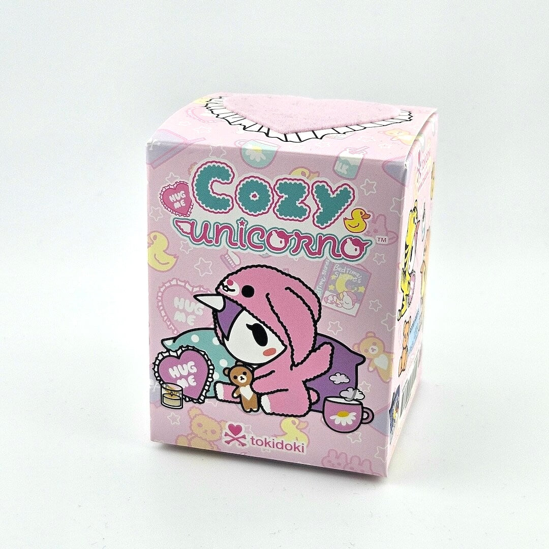 Pink packaging box with cartoon character and 'Cozy Unicorno' text on a light gray background