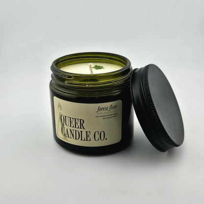 Green glass jar with black lid containing candle with label against white background.