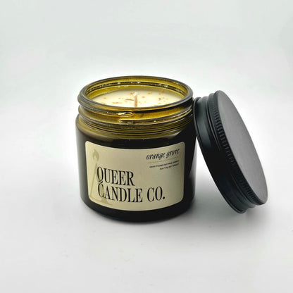 Green glass jar with black lid containing candle with label against white background.