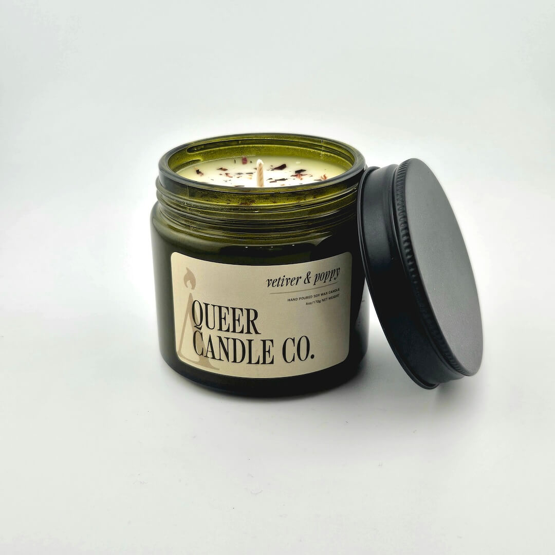 Green glass jar with black lid containing candle with label against white background.