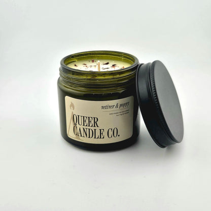 Green glass jar with black lid containing candle with label against white background.